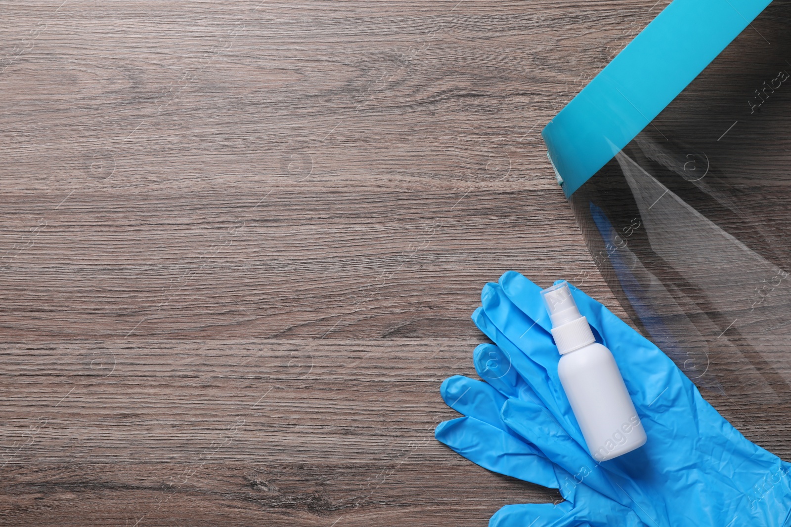 Photo of Face shield, medical gloves and antiseptic on wooden background, flat lay with space for text. Personal safety equipment