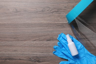 Photo of Face shield, medical gloves and antiseptic on wooden background, flat lay with space for text. Personal safety equipment