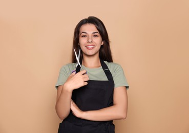 Photo of Portrait of happy hairdresser with professional scissors against pale orange background