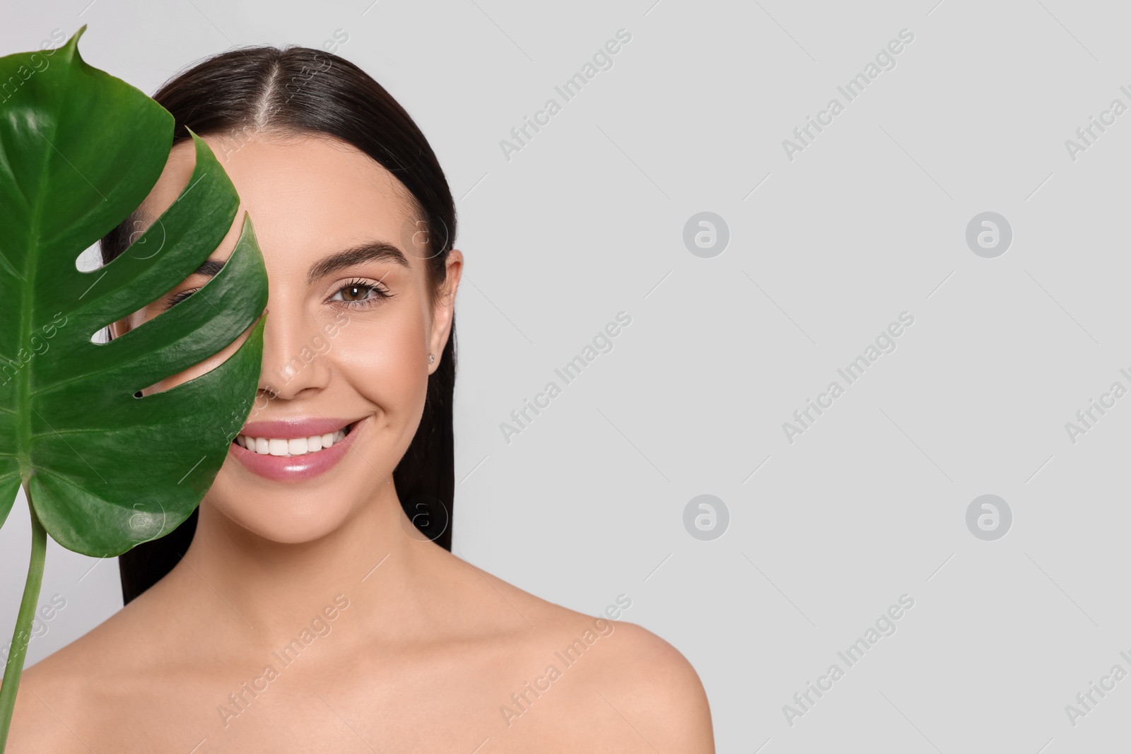 Photo of Woman holding leaf of monstera on light grey background, space for text. Spa treatment