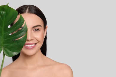 Photo of Woman holding leaf of monstera on light grey background, space for text. Spa treatment