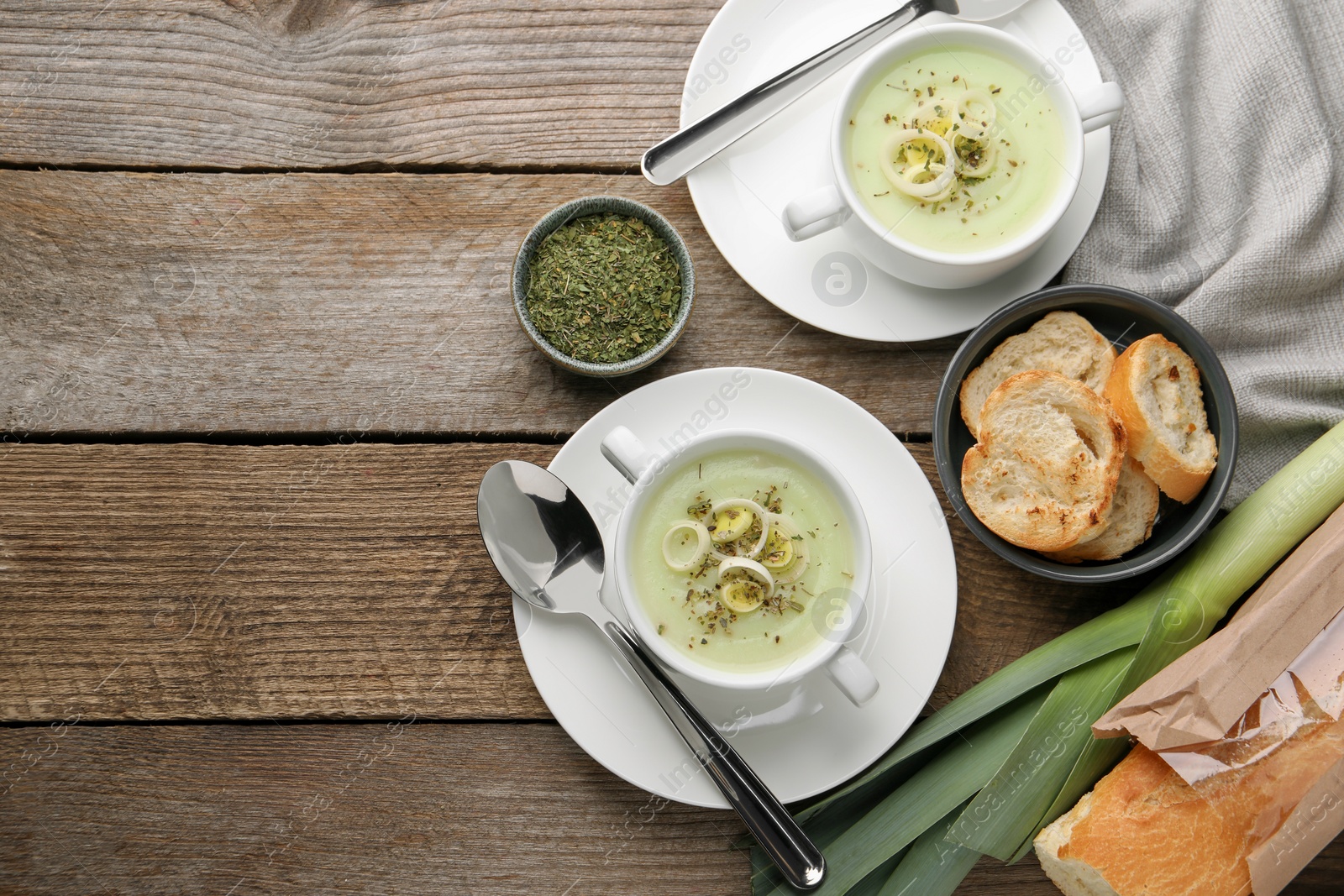 Photo of Delicious cream soup with leek and spices served on wooden table, flat lay. Space for text