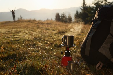 Photo of Camping burner with mug of hot drink near backpack on grass in mountains. Space for text