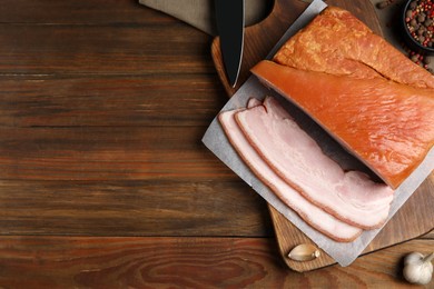 Photo of Delicious smoked bacon and garlic on wooden table, flat lay. Space for text