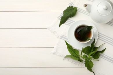 Aromatic nettle tea and green leaves on white wooden table, flat lay. Space for text