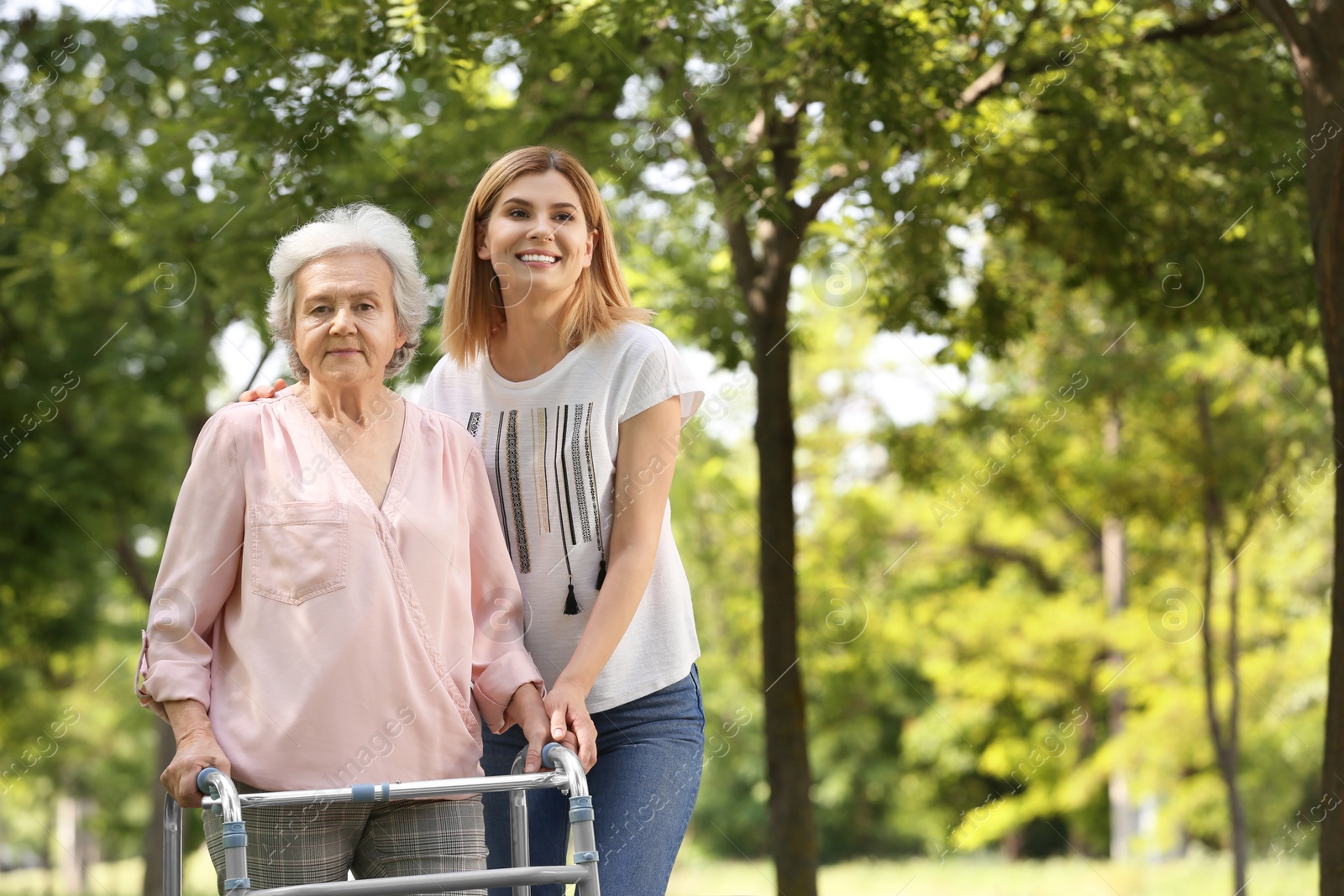 Photo of Caretaker helping elderly woman with walking frame outdoors