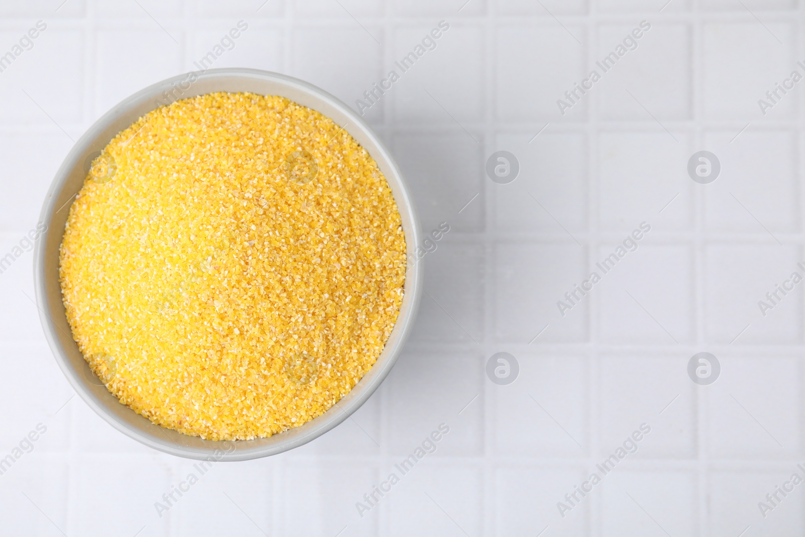 Photo of Raw cornmeal in bowl on white tiled table, top view. Space for text