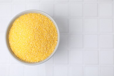 Raw cornmeal in bowl on white tiled table, top view. Space for text