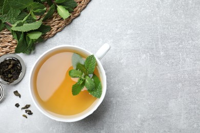 Photo of Cup of aromatic green tea with mint and dry leaves on grey table, flat lay. Space for text