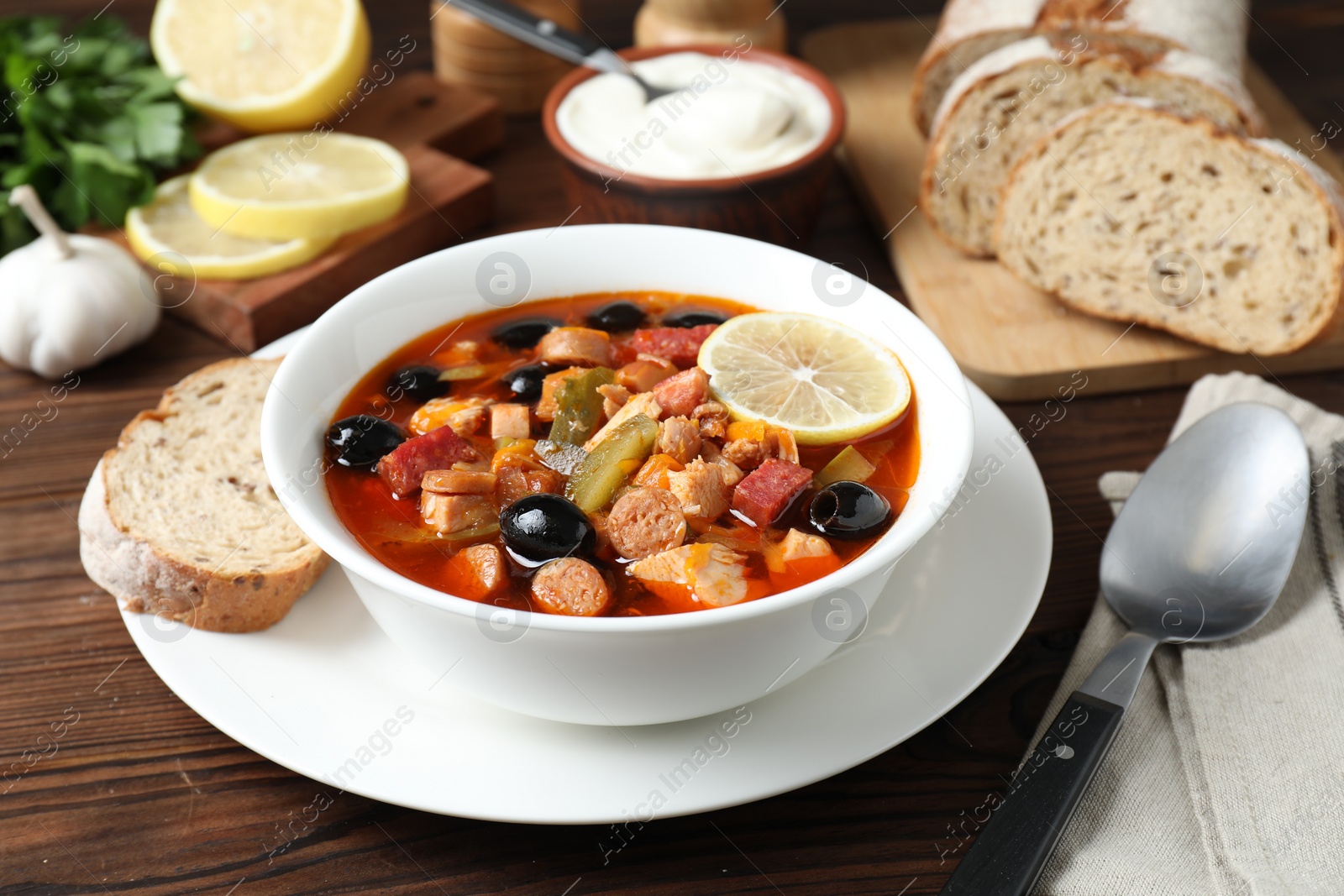 Photo of Meat solyanka soup with sausages, olives and vegetables served on wooden table