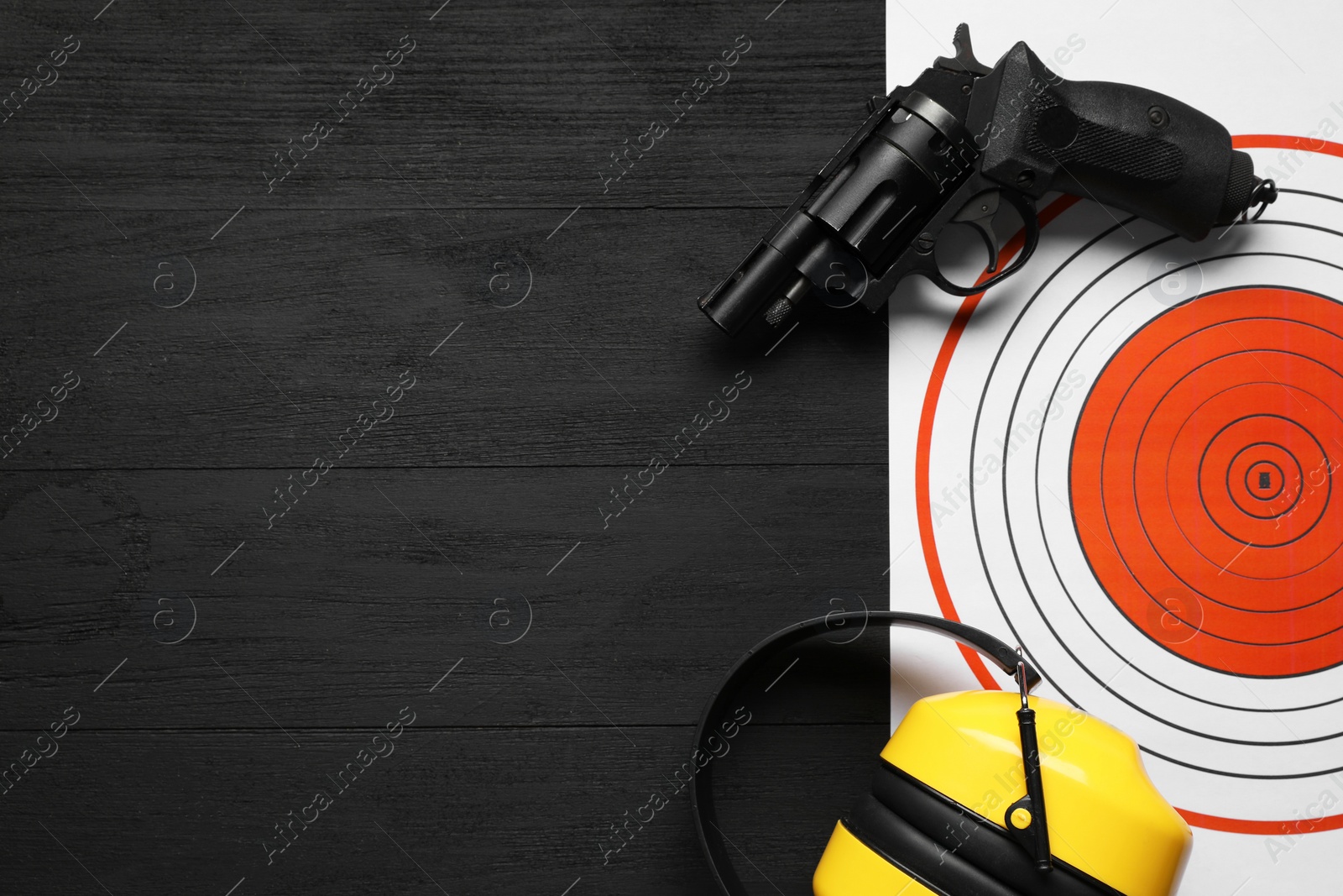 Photo of Shooting target, handgun and headphones on black wooden table, top view. Space for text