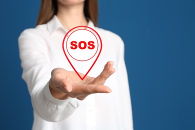 Young woman holding virtual icon SOS on blue background, closeup