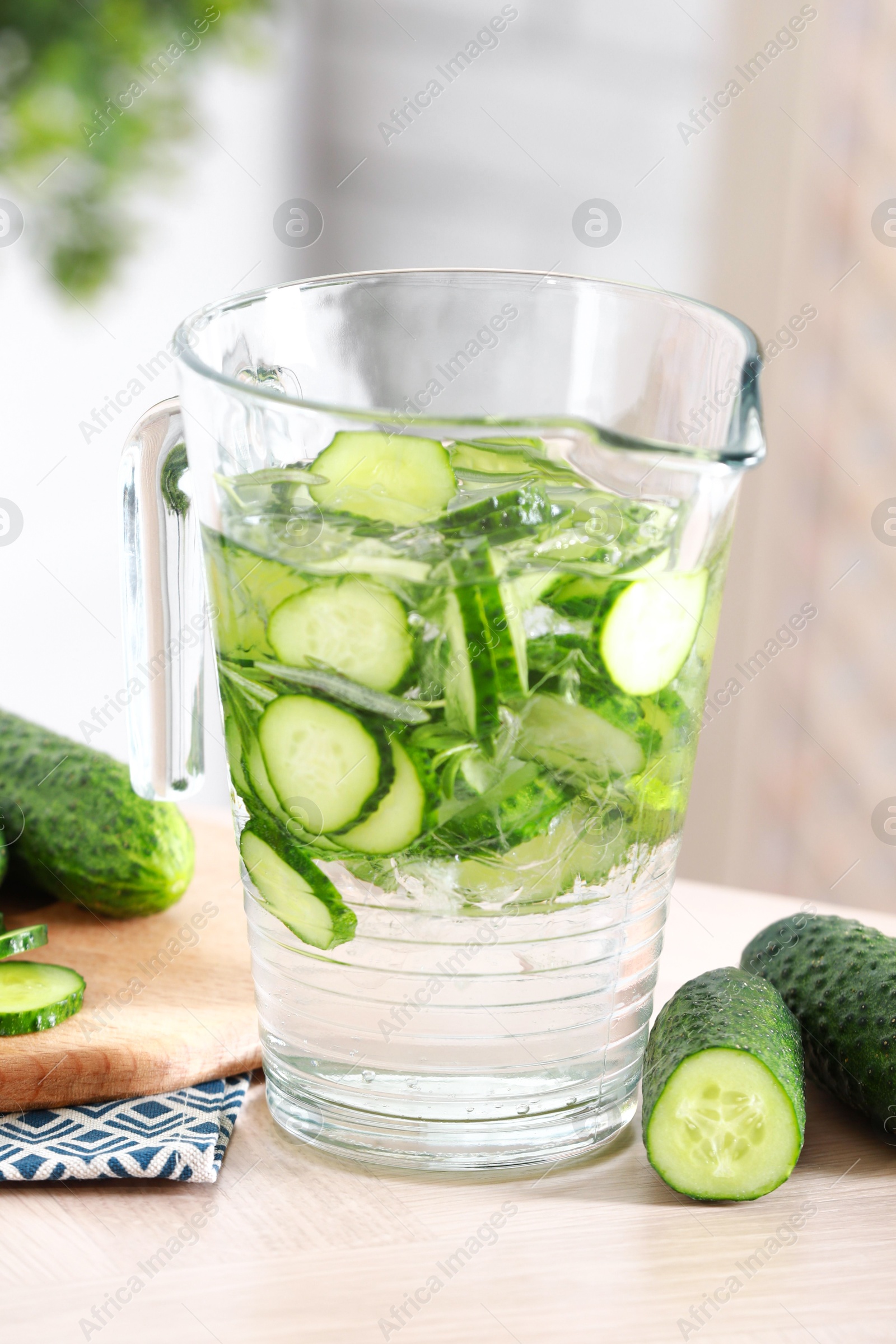 Photo of Refreshing cucumber water in jug and vegetables on light wooden table