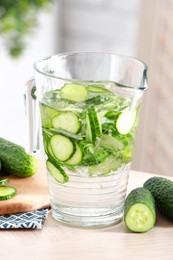 Refreshing cucumber water in jug and vegetables on light wooden table