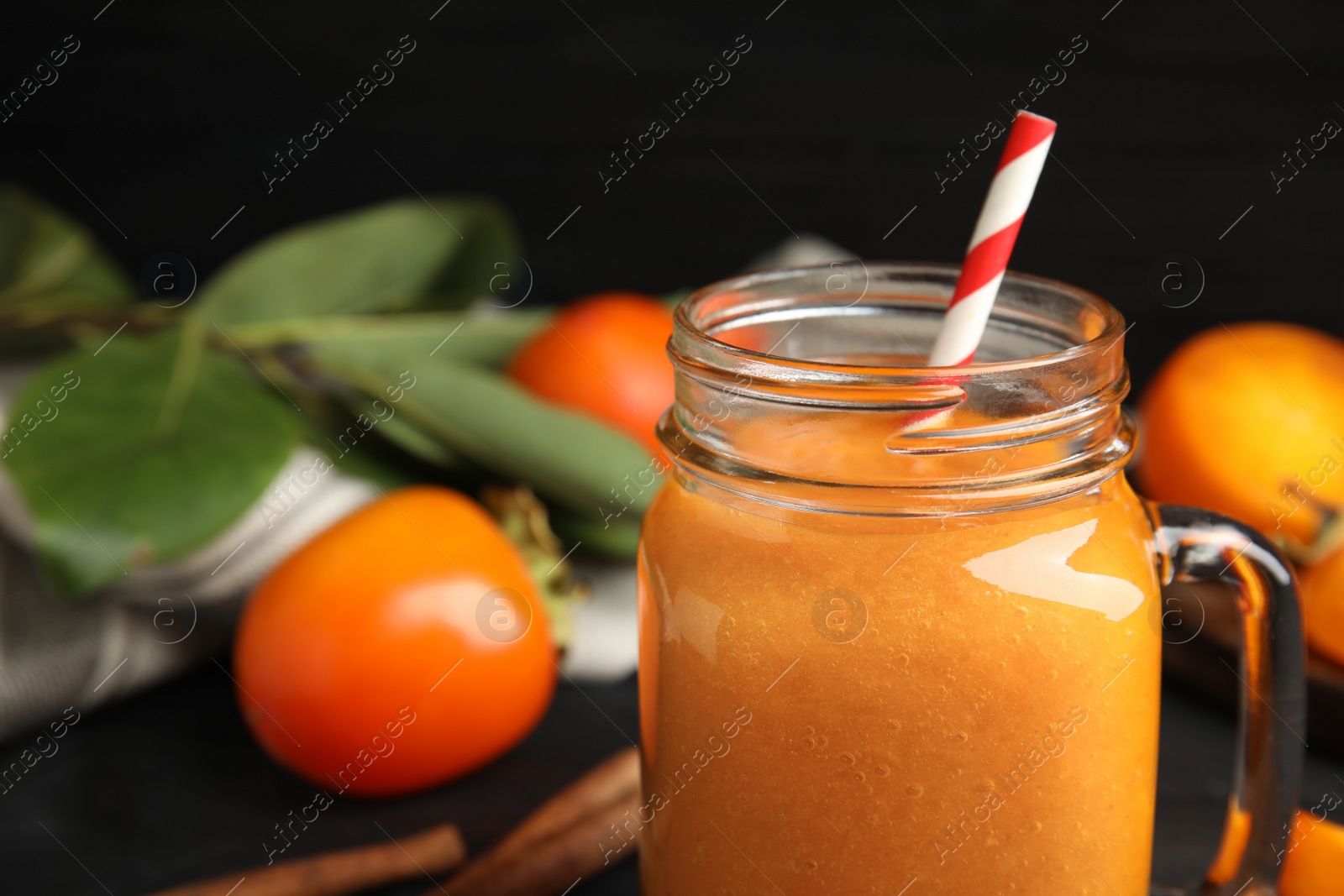 Photo of Tasty persimmon smoothie with straw in mason jar, closeup. Space for text