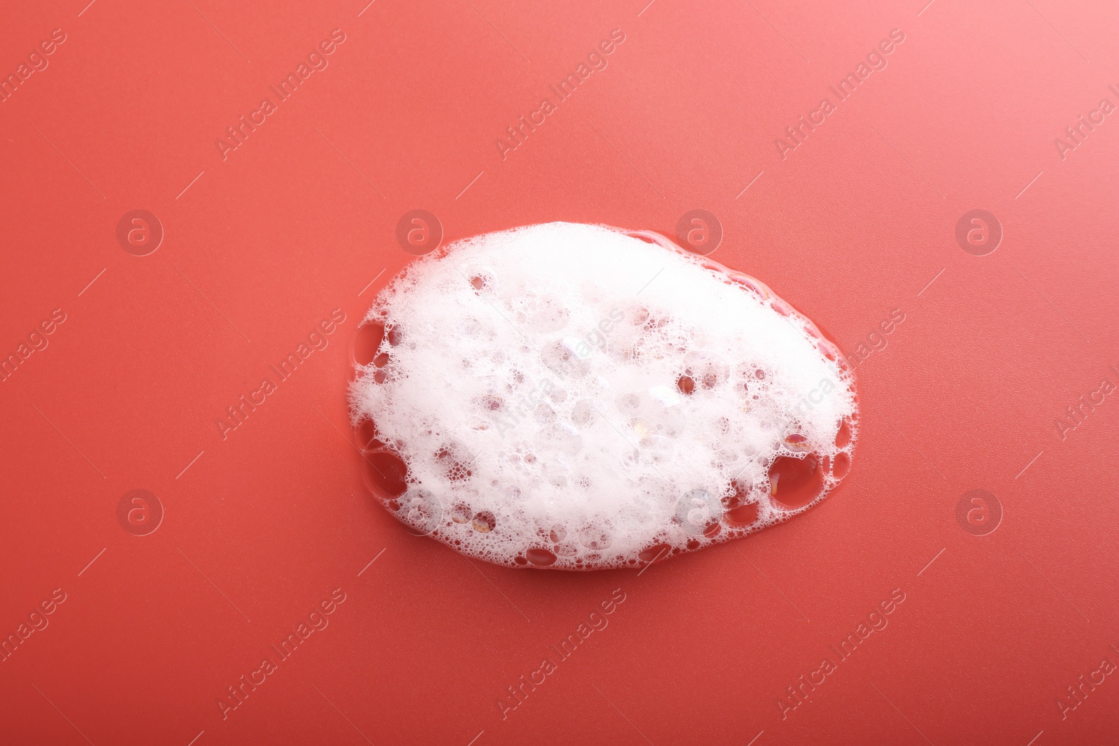 Photo of White foam with bubbles on red background, top view