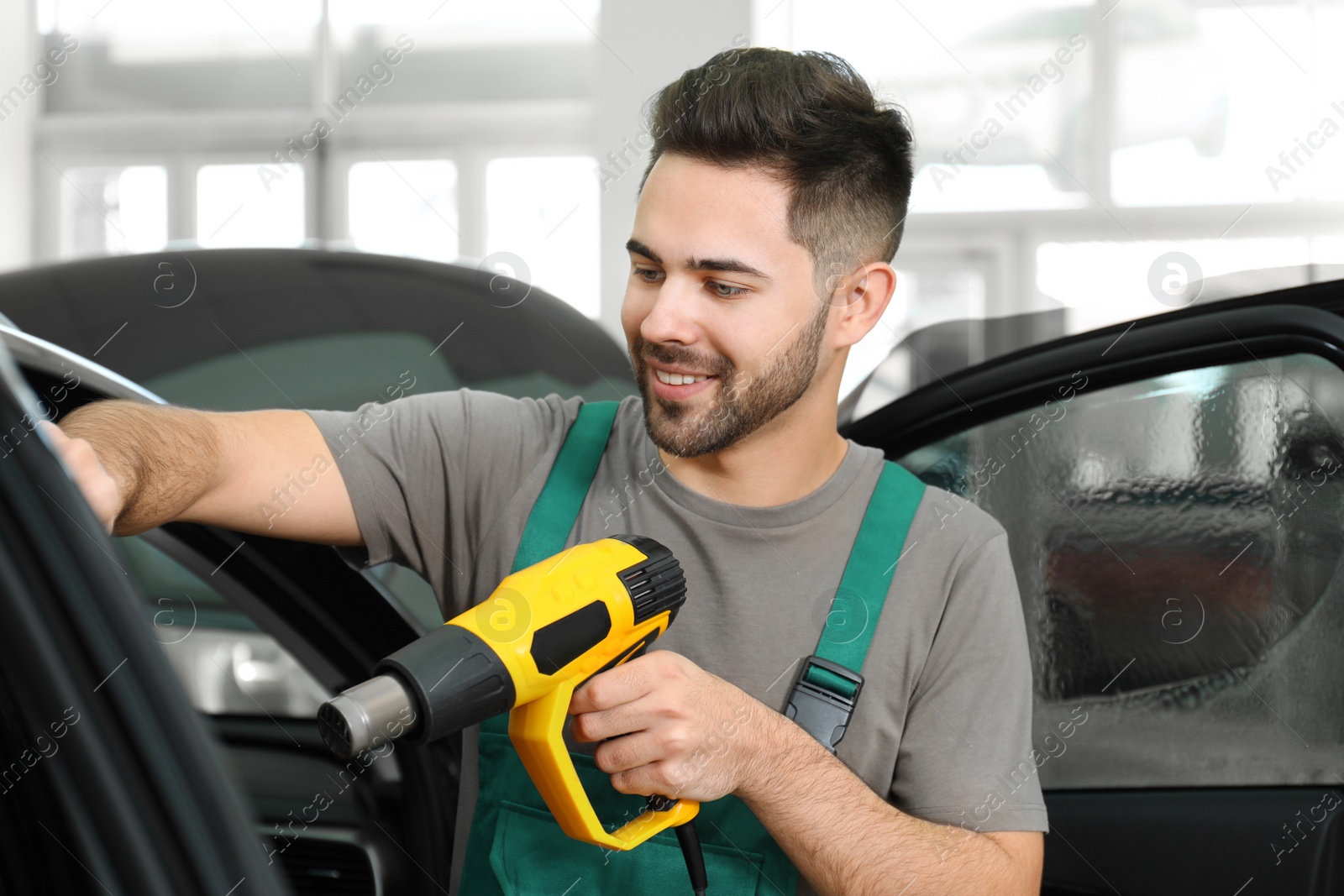 Photo of Worker tinting car window with heat gun in workshop