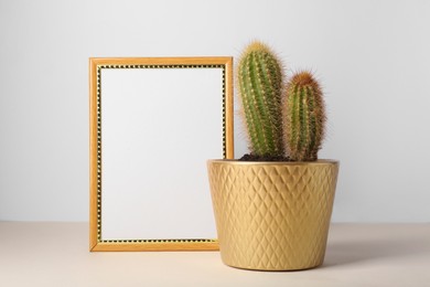 Beautiful cactus in pot and frame on beige table