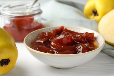 Photo of Tasty homemade quince jam in bowl and fruits on white wooden table, closeup