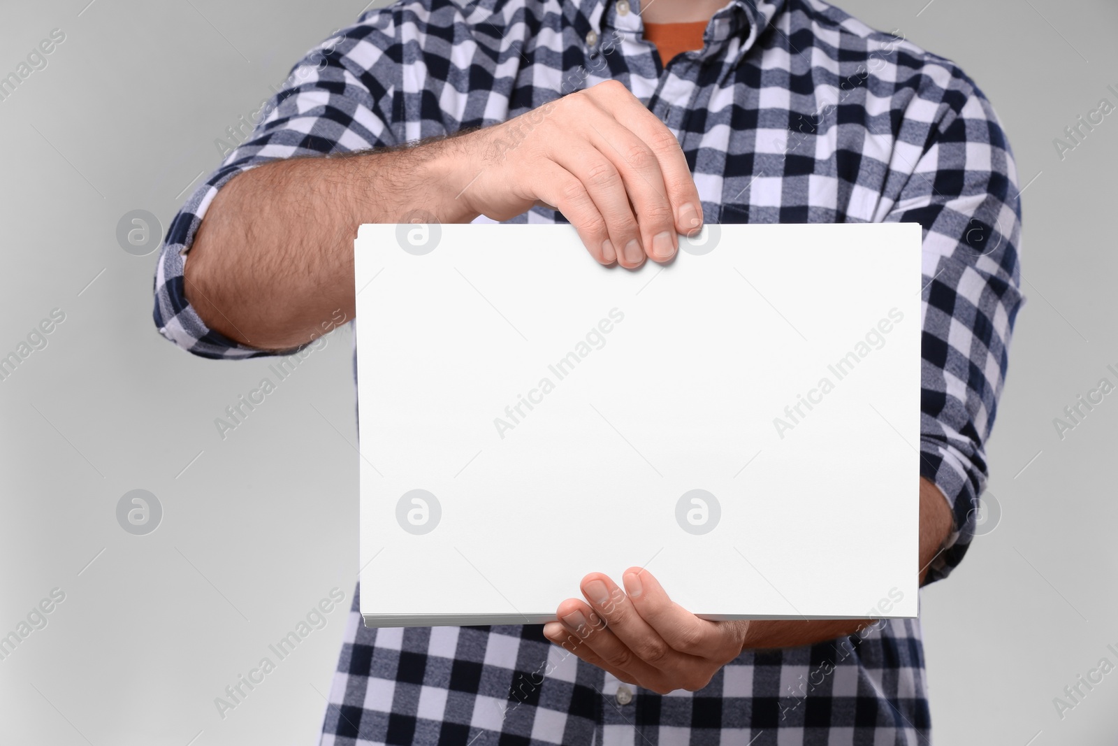 Photo of Man holding sheet of paper on light grey background, closeup. Mockup for design