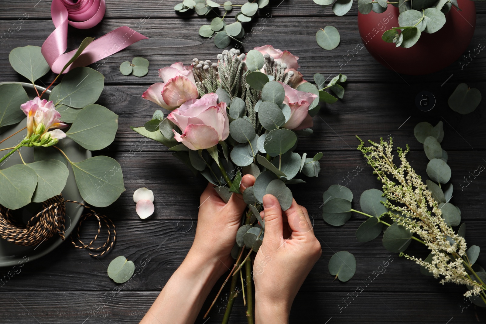 Photo of Florist creating beautiful bouquet at black wooden table, top view