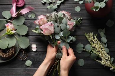 Photo of Florist creating beautiful bouquet at black wooden table, top view