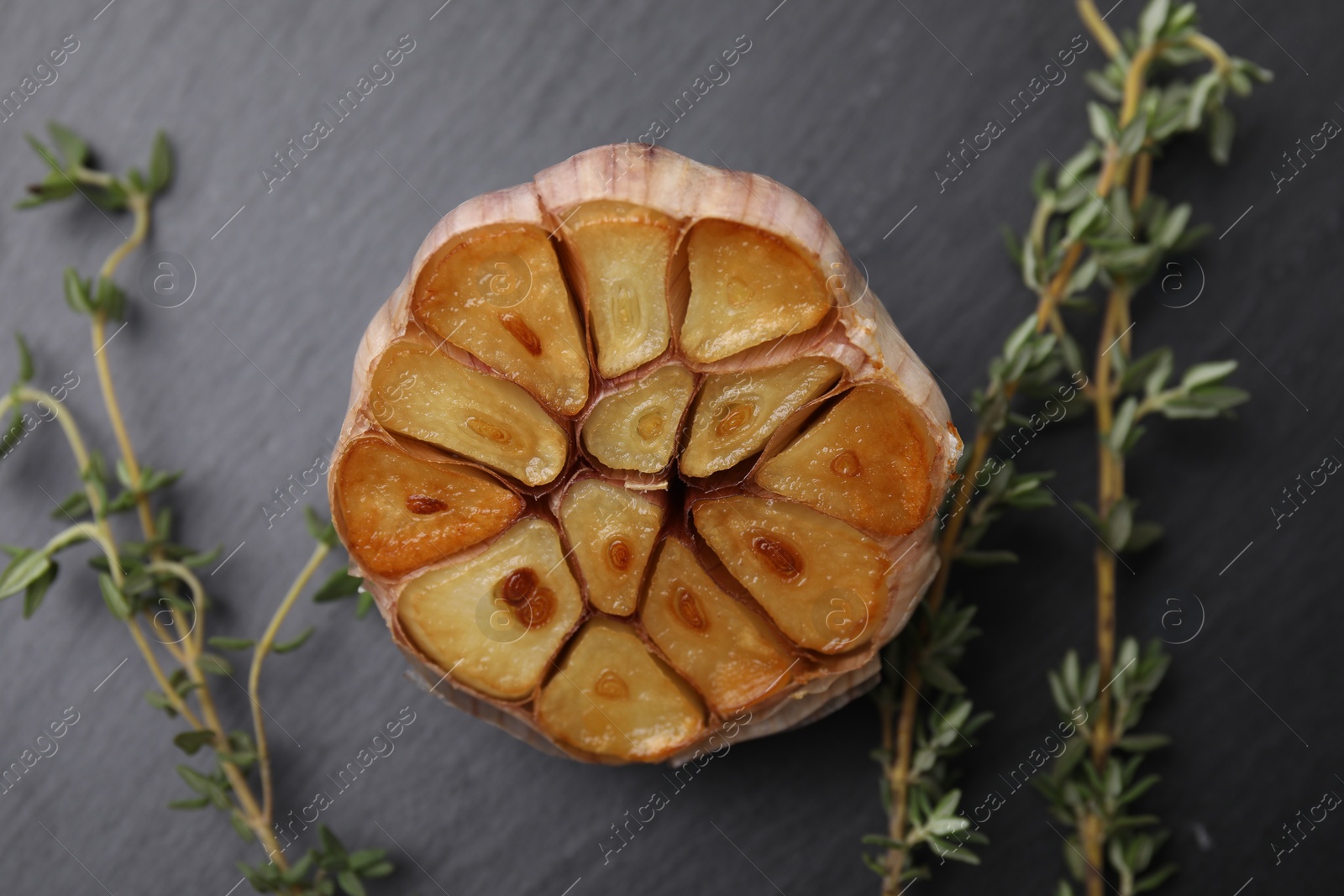 Photo of Head of fried garlic and thyme on dark gray table, closeup
