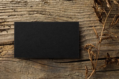 Empty black business card and dried plant on wooden background, top view. Mockup for design