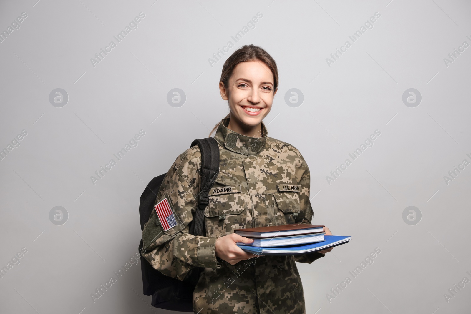 Photo of Female cadet with backpack and books on light grey background. Military education