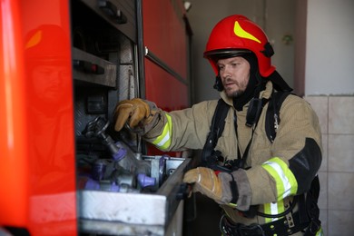 Photo of Firefighter in uniform with fire engine equipment at station