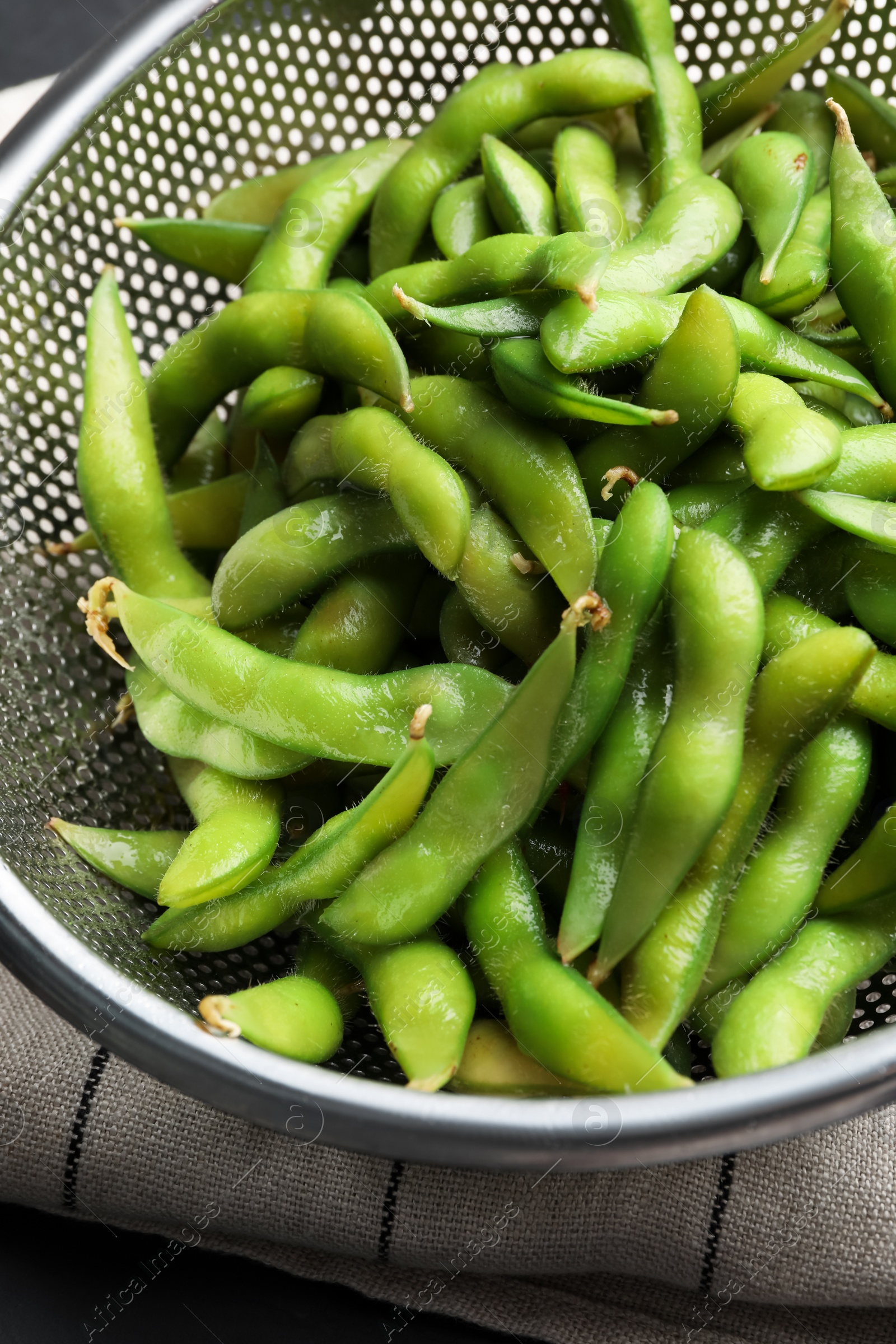 Photo of Sieve with green edamame beans in pods on table, closeup