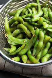 Sieve with green edamame beans in pods on table, closeup
