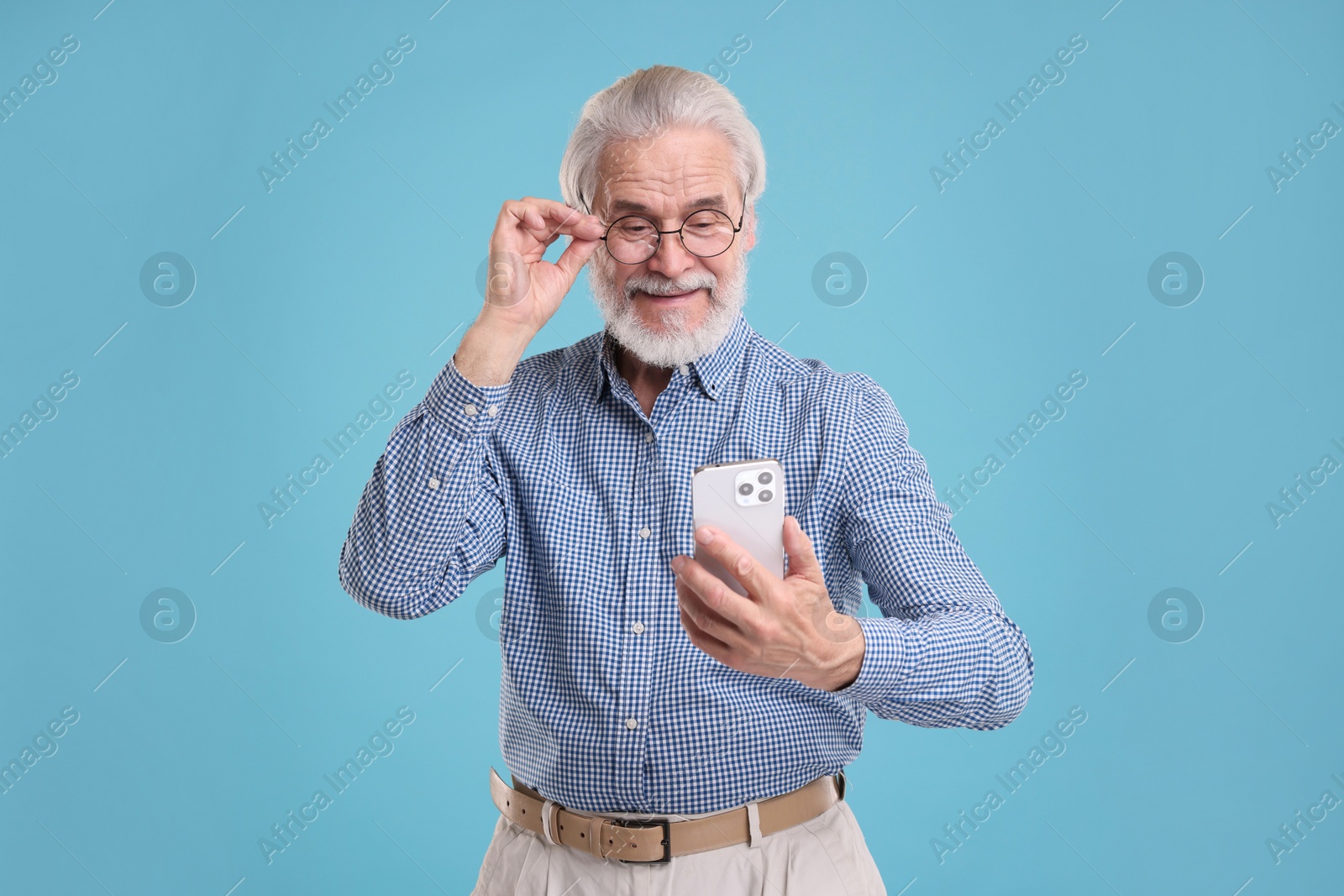 Photo of Portrait of stylish grandpa with glasses using smartphone on light blue background