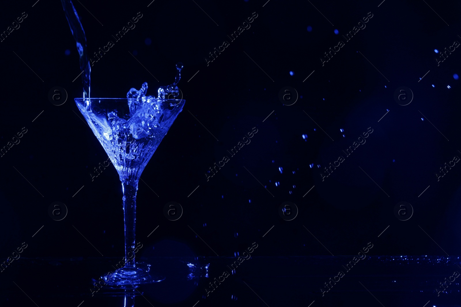 Photo of Pouring martini. Glass and splashes on dark blue background, bokeh effect with space for text