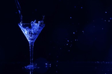 Photo of Pouring martini. Glass and splashes on dark blue background, bokeh effect with space for text