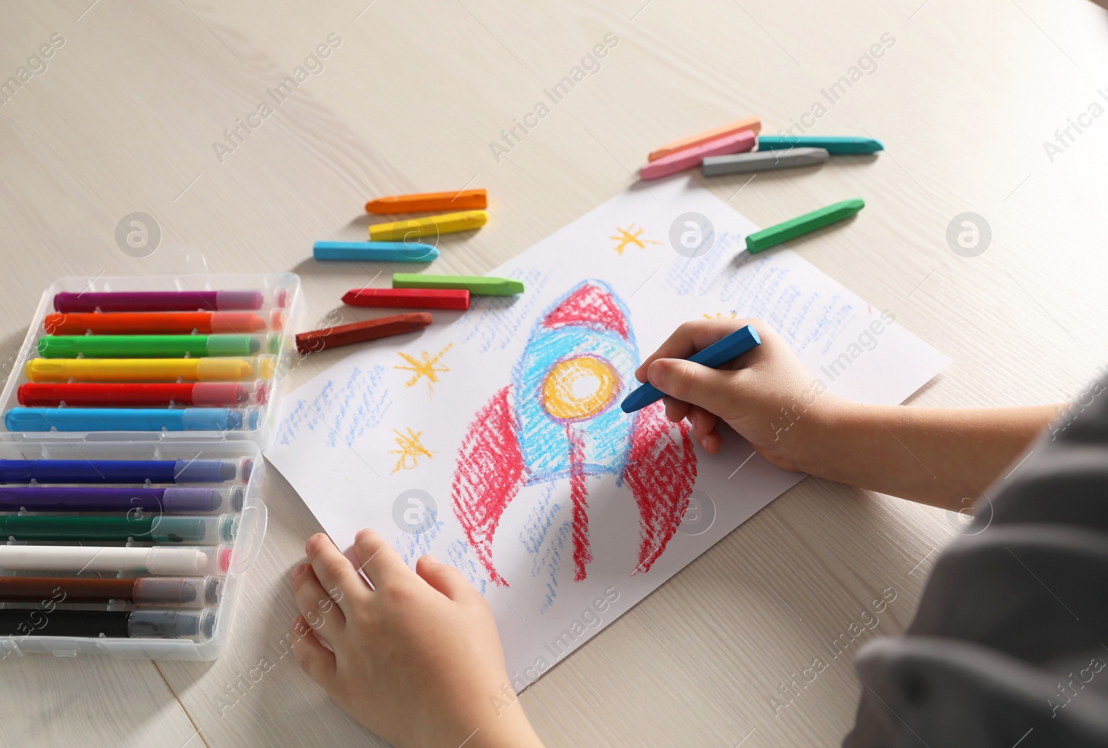 Photo of Little boy drawing rocket with soft pastel at wooden table, closeup. Child`s art