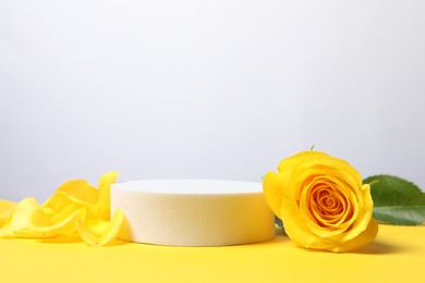 Beautiful presentation for product. Round podium and rose on yellow table against white background, space for text