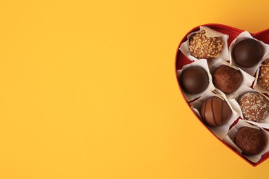 Photo of Heart shaped box with delicious chocolate candies on yellow background, top view. Space for text
