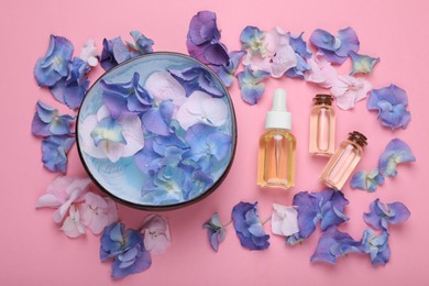 Spa composition. Aromatic water in bowl, flowers and bottles of essential oil on pink background, flat lay