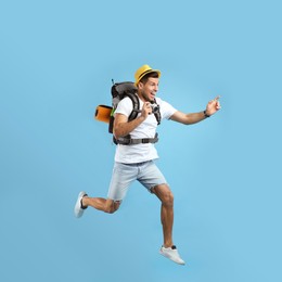 Photo of Emotional male tourist with travel backpack and camera jumping on turquoise background