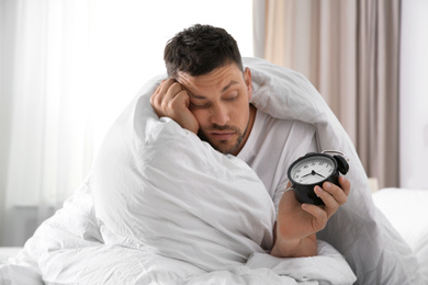 Photo of Sleepy man with alarm clock at home in morning