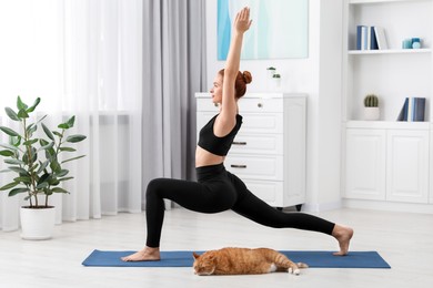 Photo of Beautiful woman with cute red cat practicing yoga on mat at home