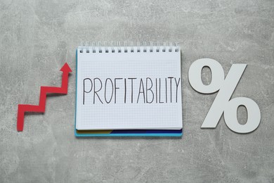 Photo of Notebook with word Profitability, percent symbol, up arrow on light grey table, top view. Profit concept