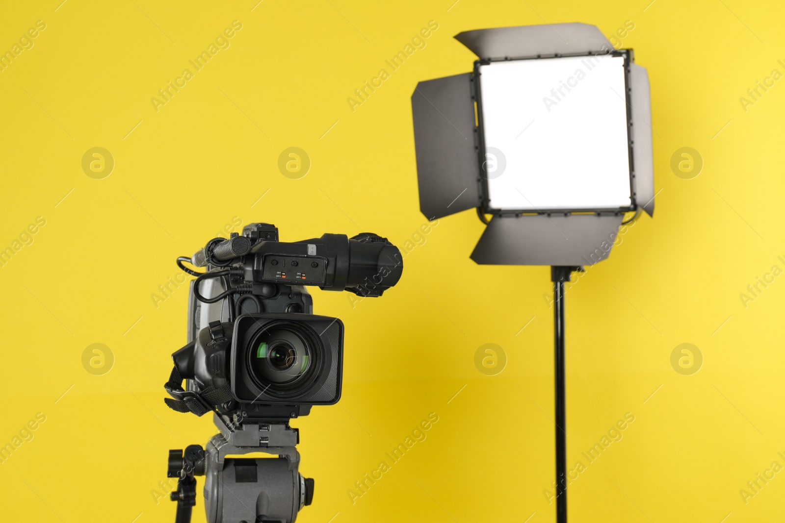 Photo of Professional video camera and lighting equipment on yellow background