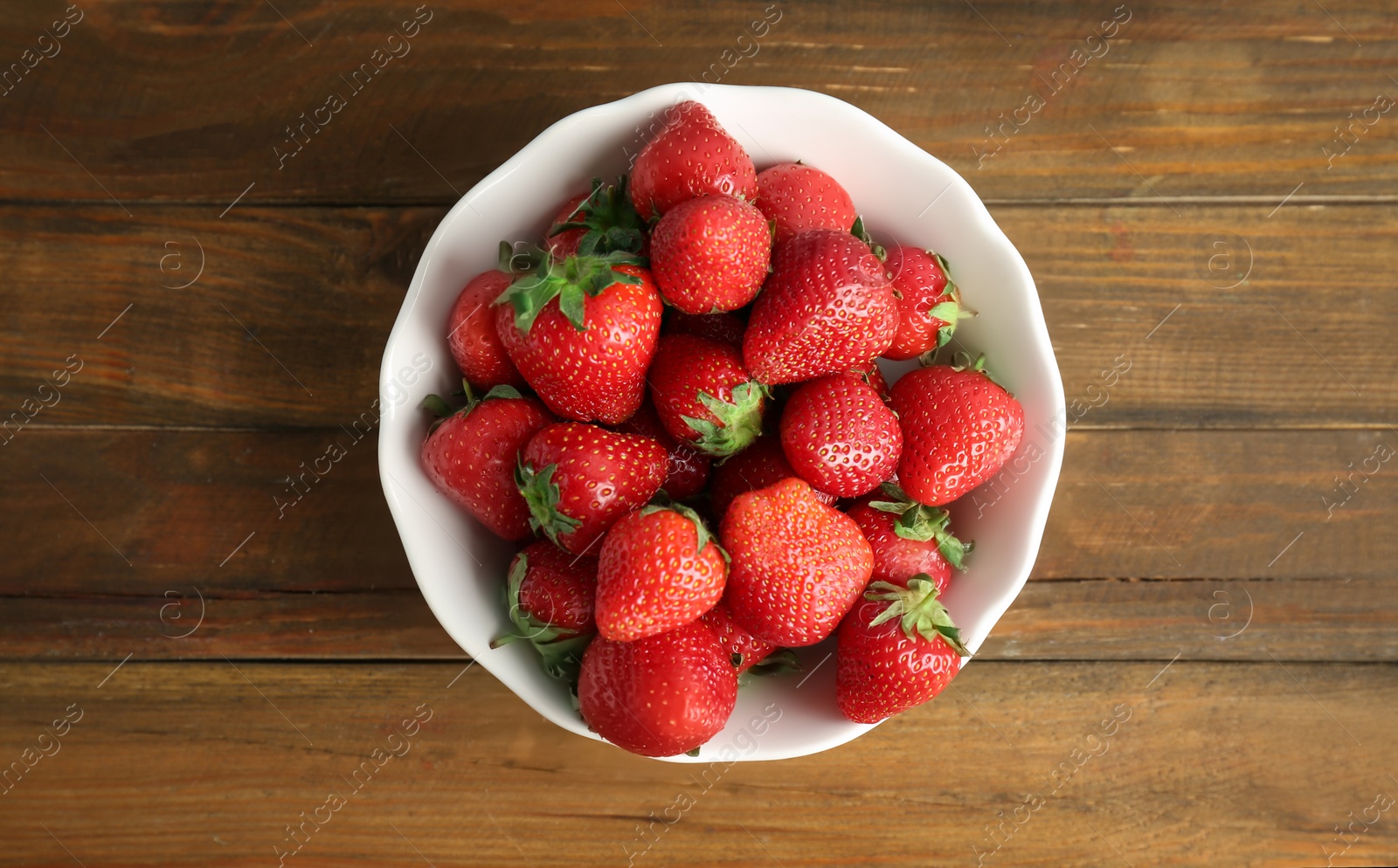 Photo of Bowl with ripe red strawberries on wooden background, top view