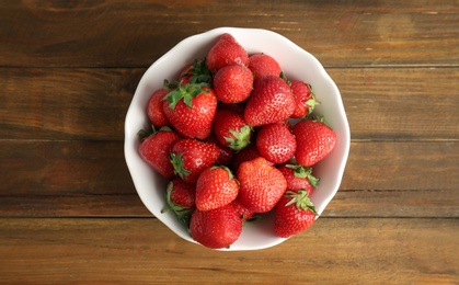 Bowl with ripe red strawberries on wooden background, top view