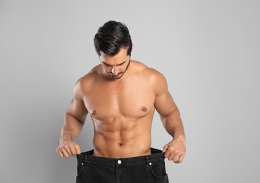 Photo of Young man with slim body in old big size jeans on grey background