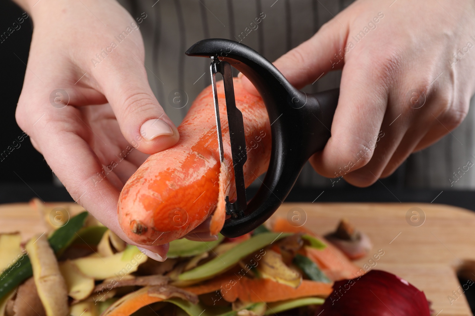 Photo of Woman peeling fresh carrot at table, closeup