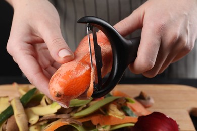 Photo of Woman peeling fresh carrot at table, closeup