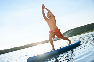 Man practicing yoga on light blue SUP board on river at sunset